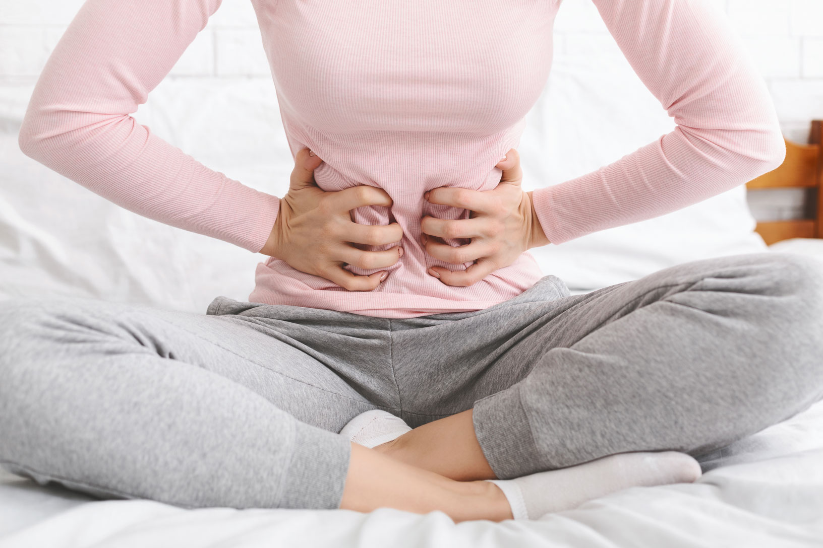 girl sitting on her bed with her two hands on her stomach