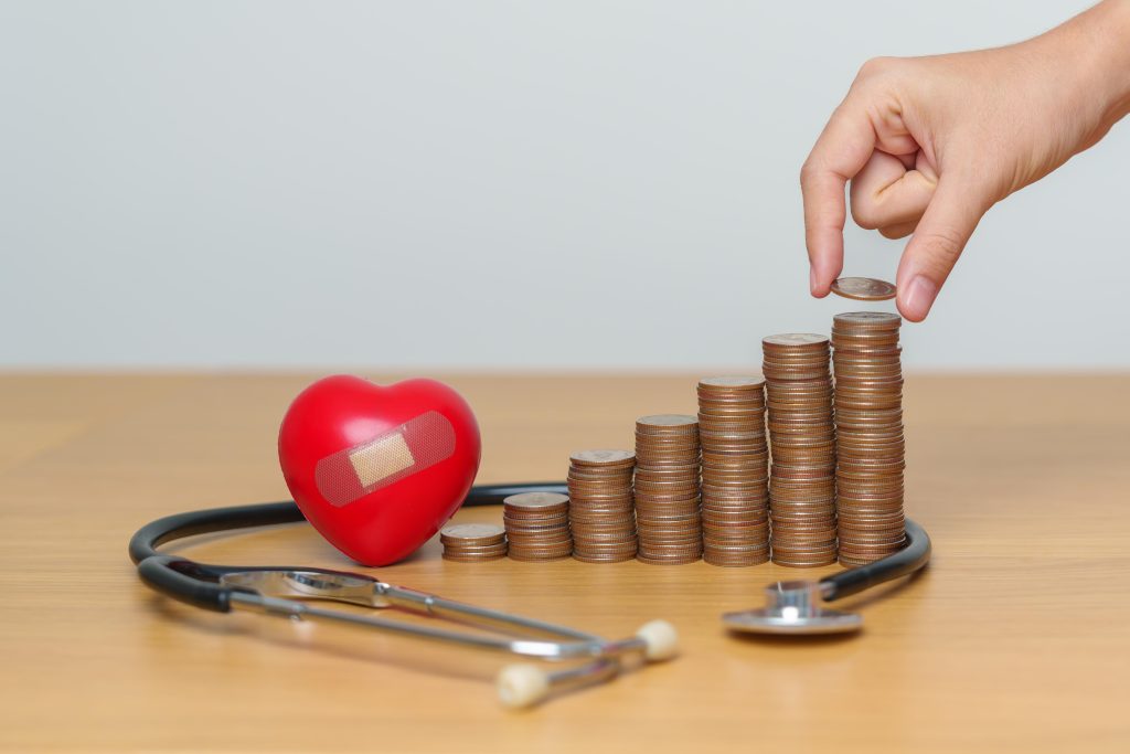 a hand stacking some coins on the table with stethoscope