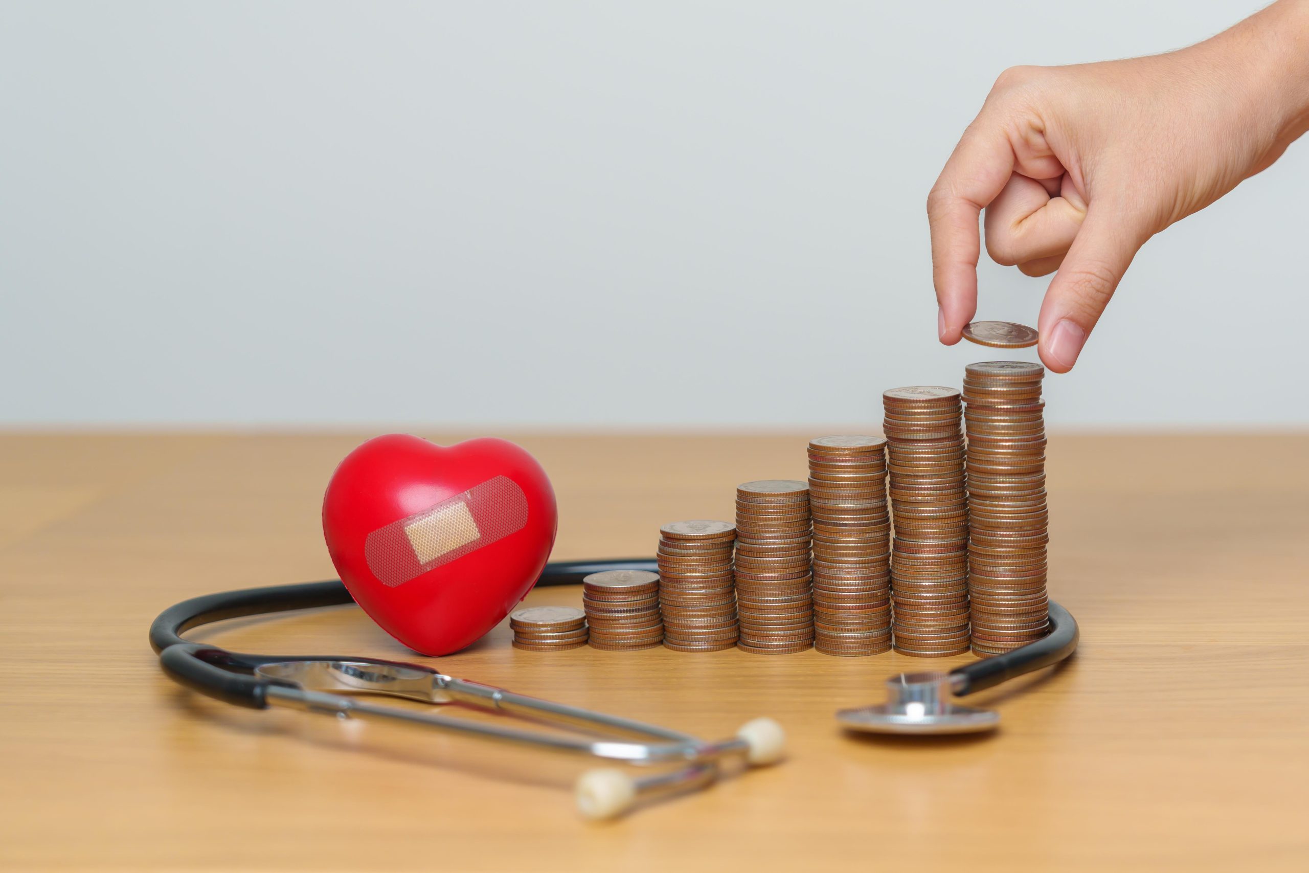 a hand stacking some coins on the table with stethoscope