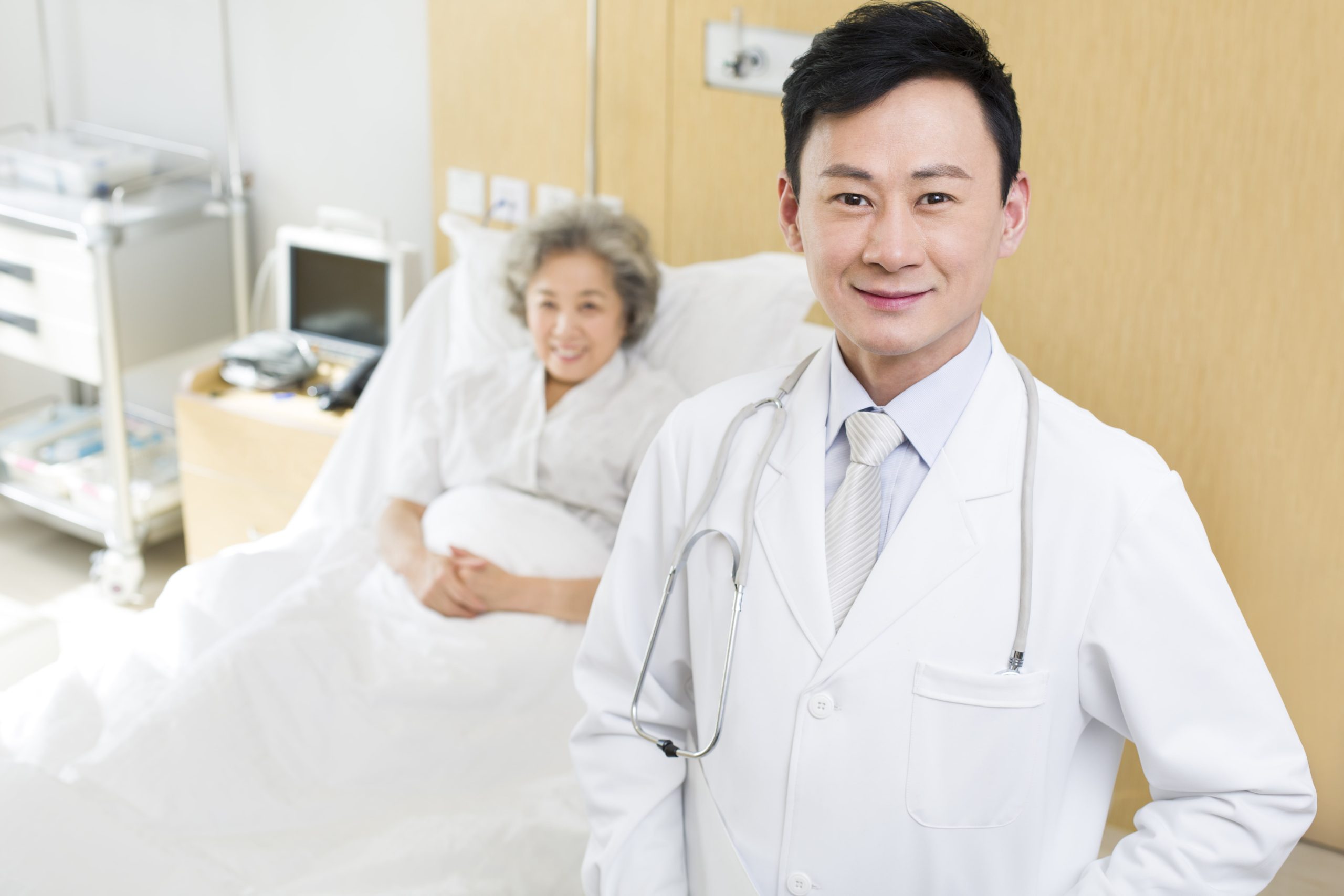 young male doctor smiling at the camera with his elderly patient behind him