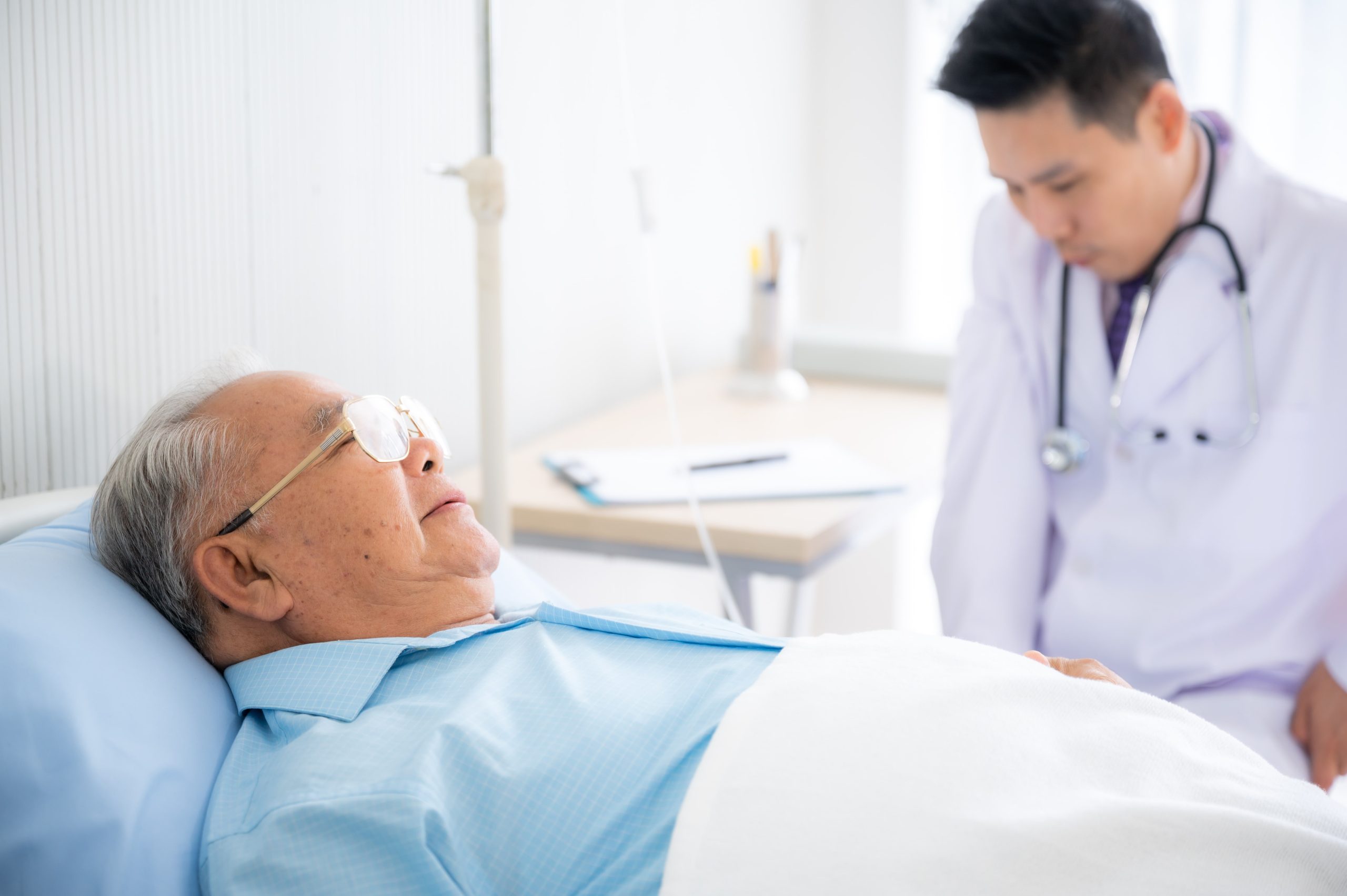 elderly patient lying in bed being attended by his doctor