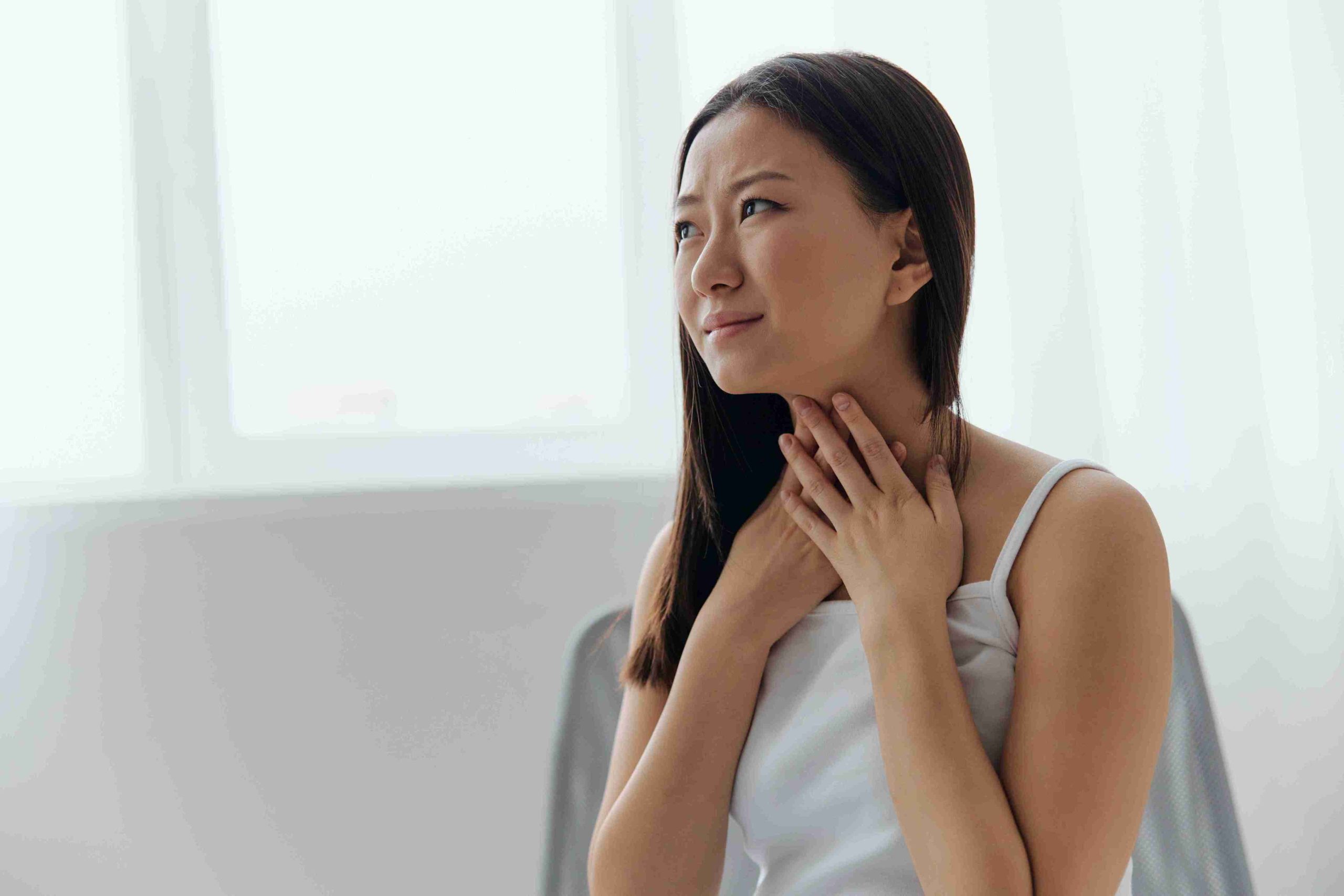 young asian woman with her hands on her throat