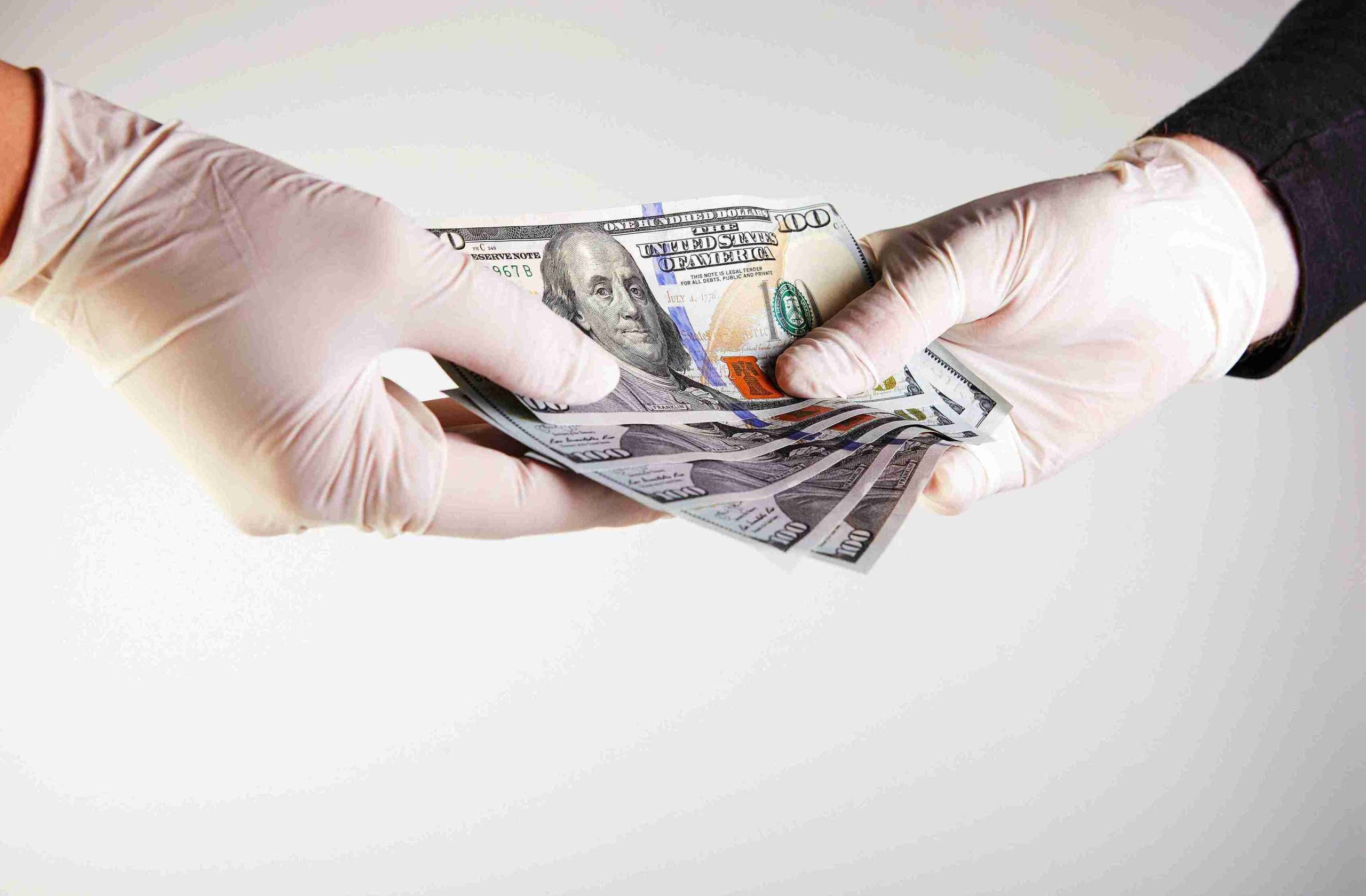 two hands wearing medical gloves exchanging money