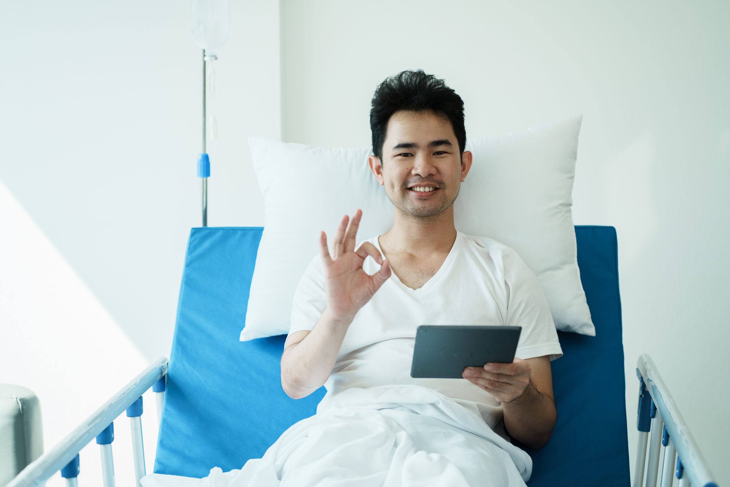 male patient sitting in a hospital bed, smiling and giving an okay sign