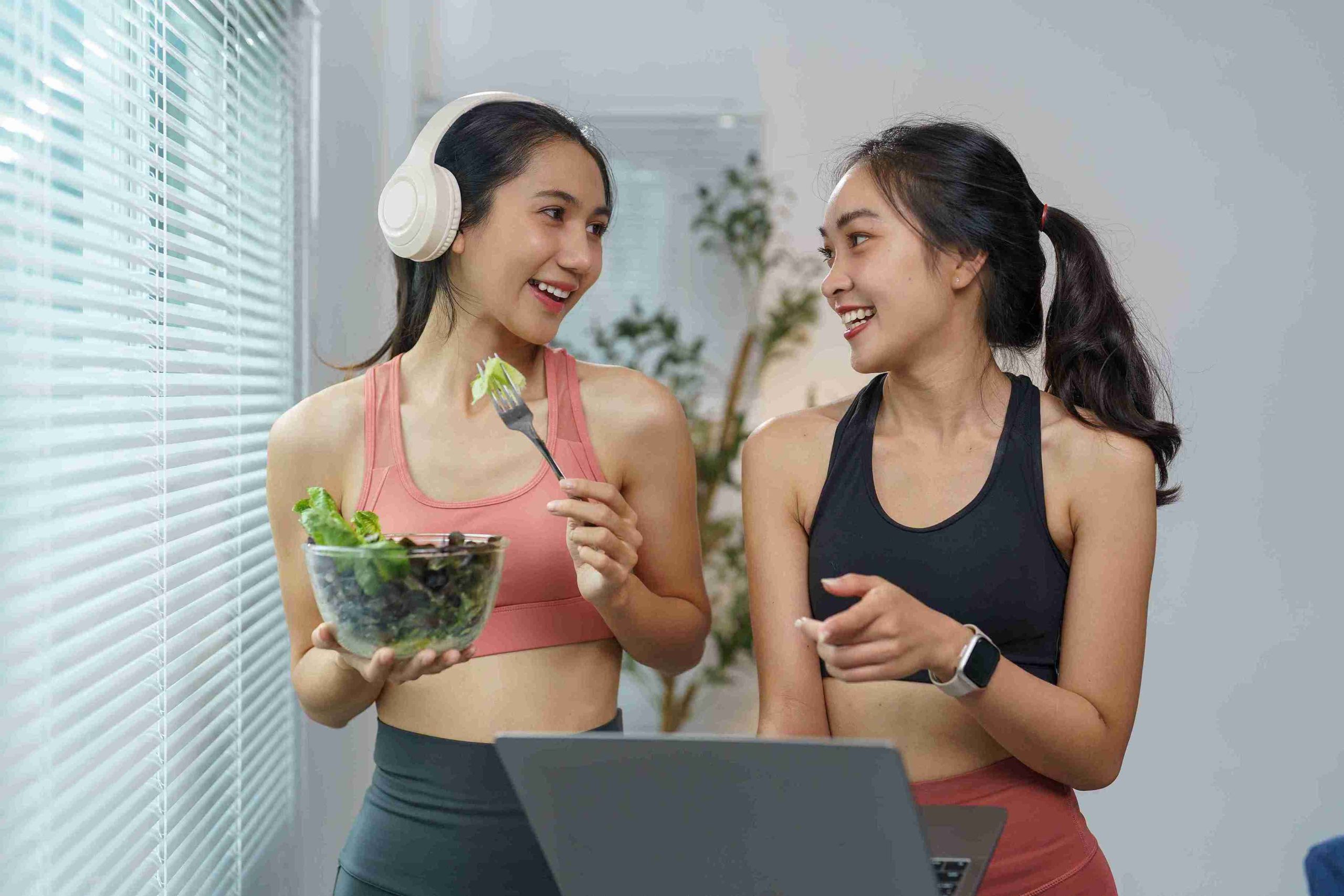 two sporty women smiling and eating salad