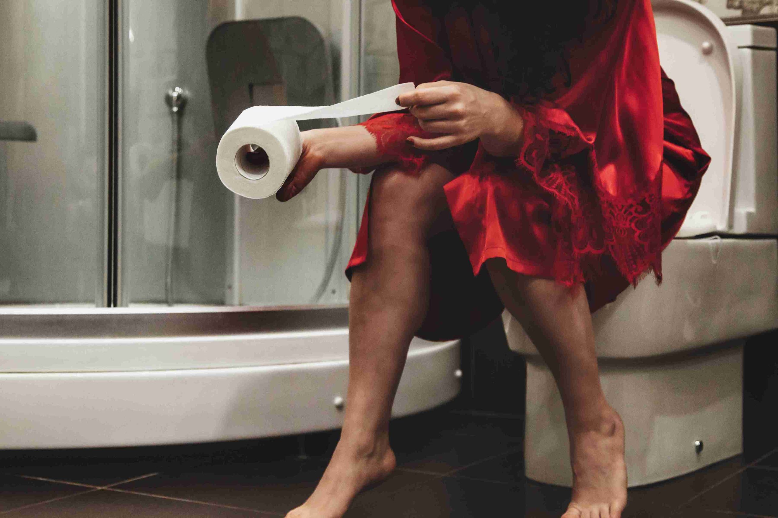 Woman sitting in the toilet bowl holding tissue paper.
