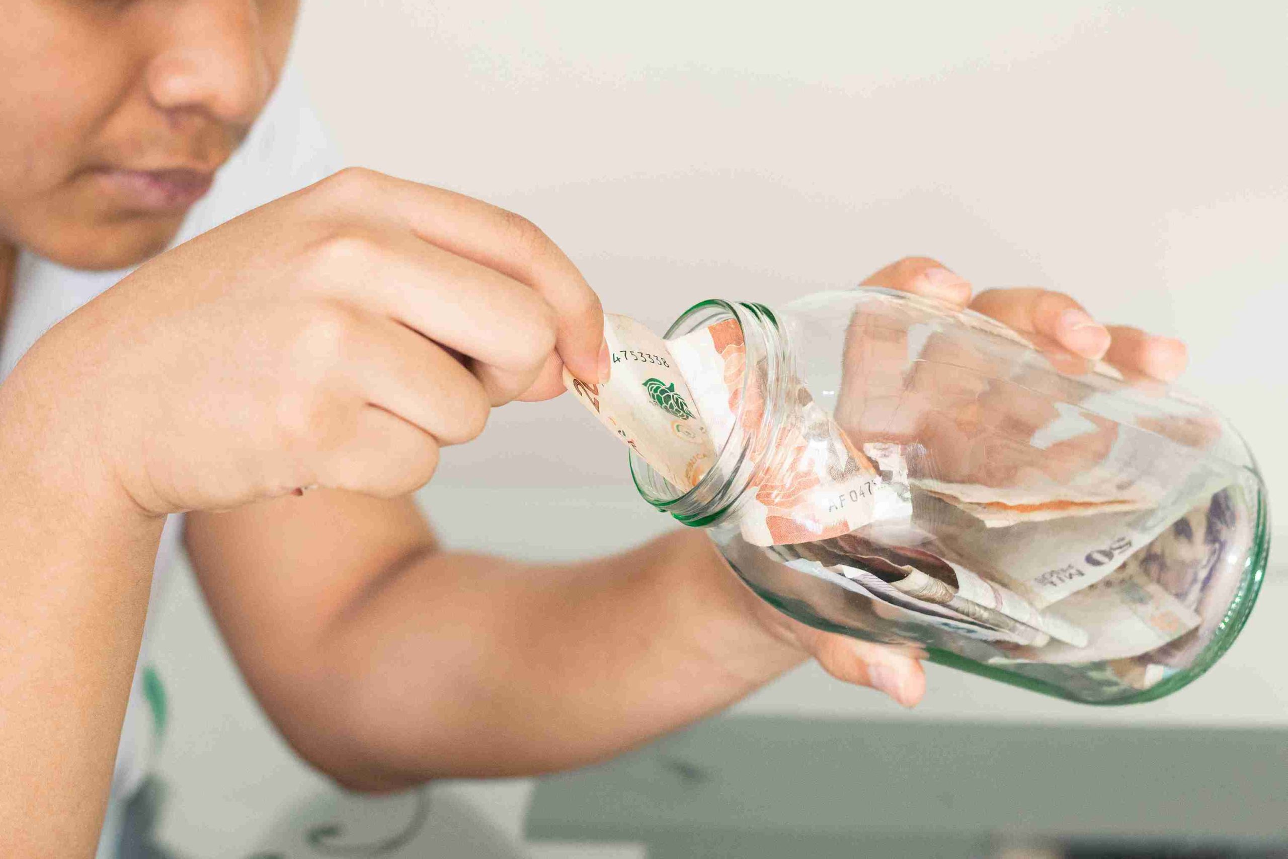 Man taking out his savings from a glass jar.