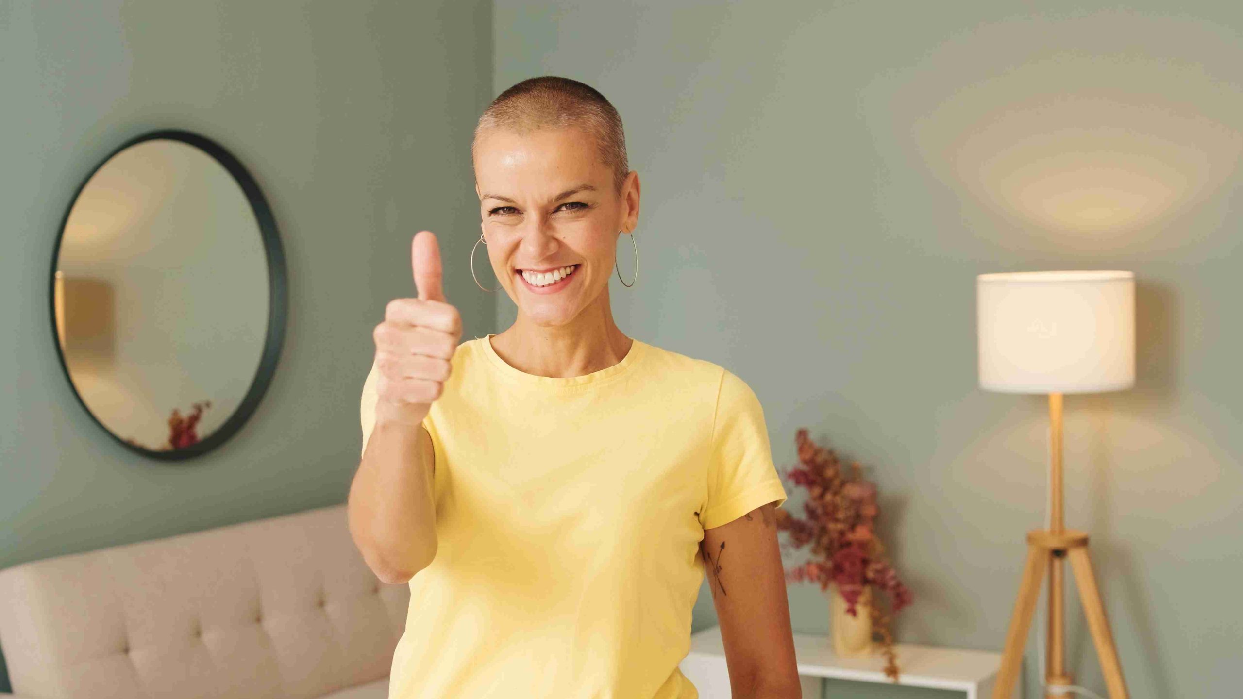 Bald woman smiling at the camera and giving a thumbs up.