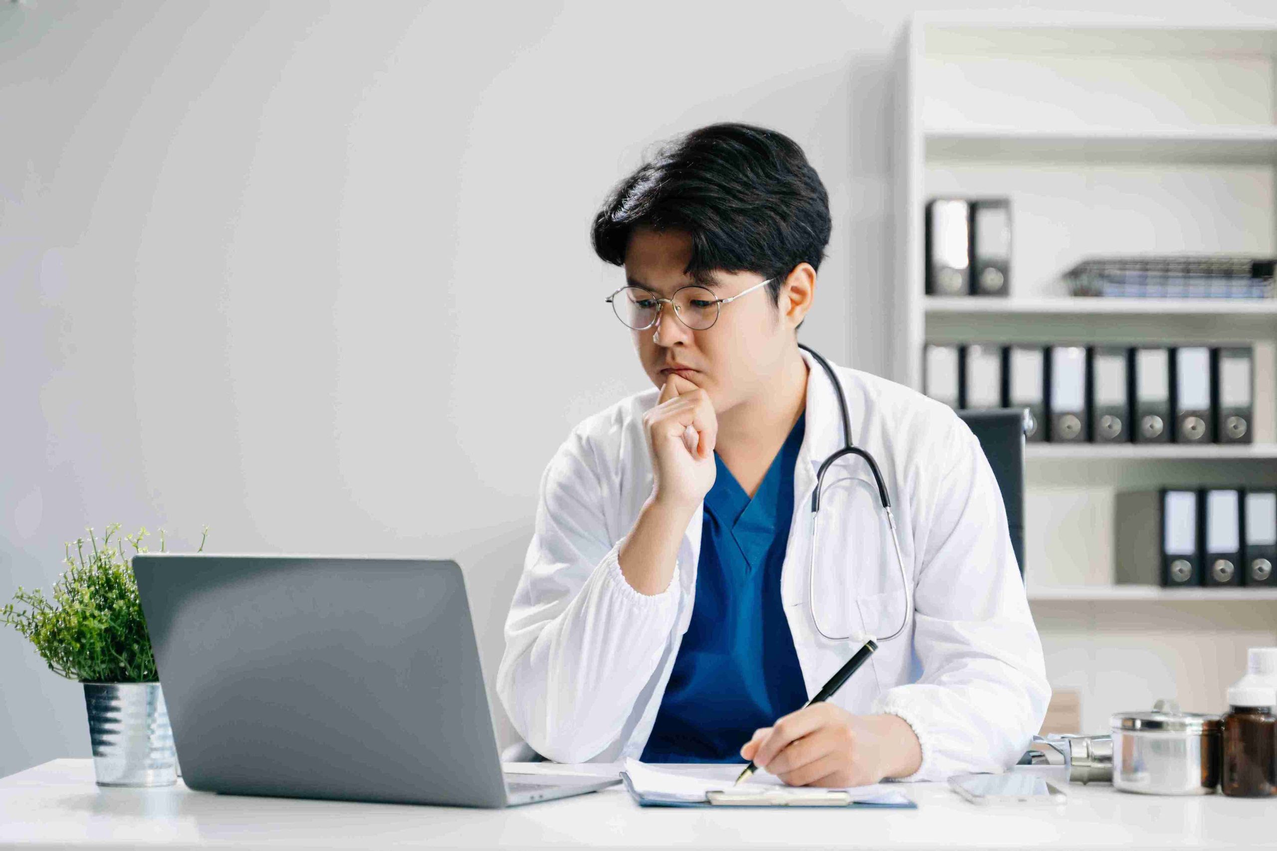 Doctor analyzing a report while looking at his laptop.