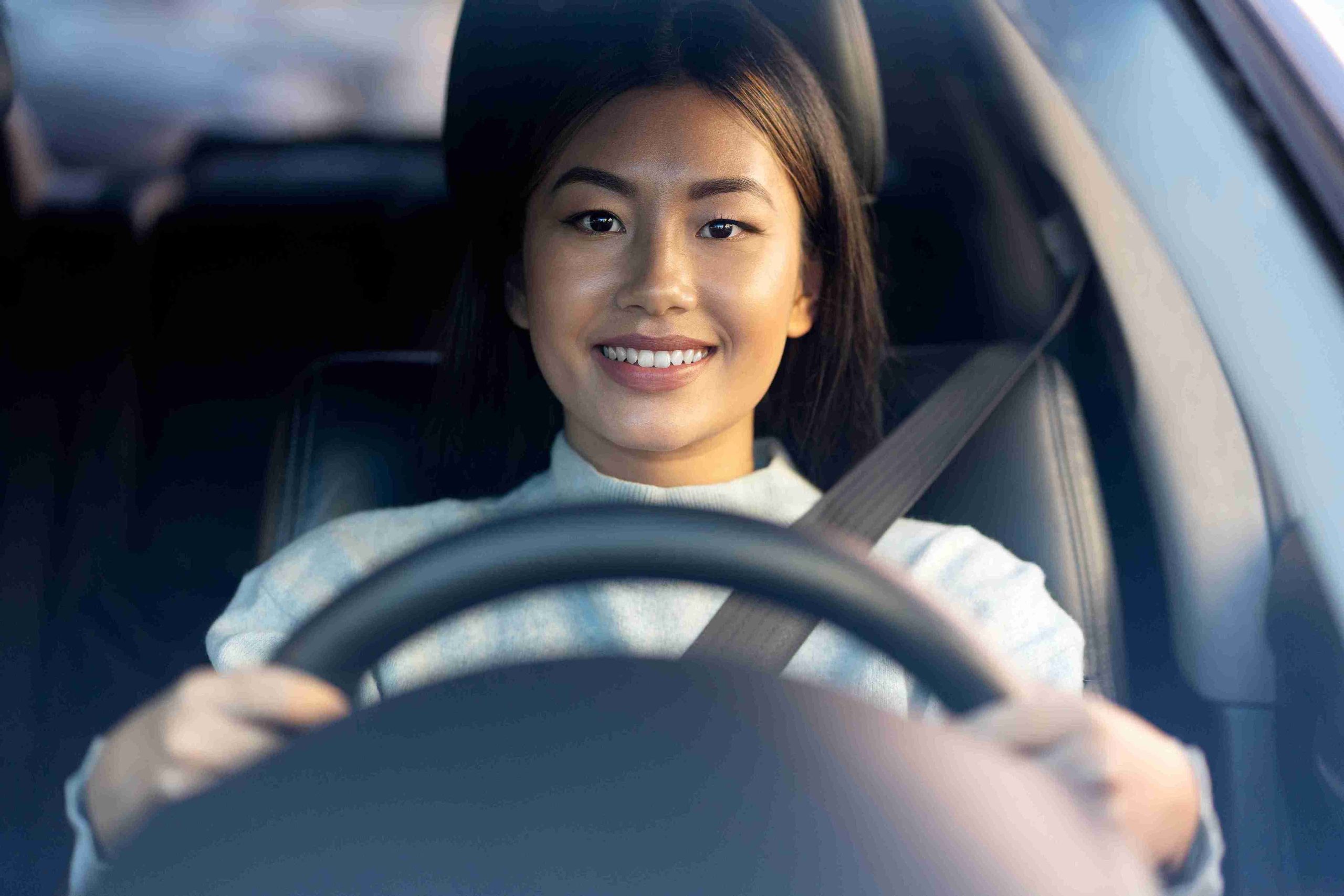 Asian woman holding the steering wheel and driving a car.