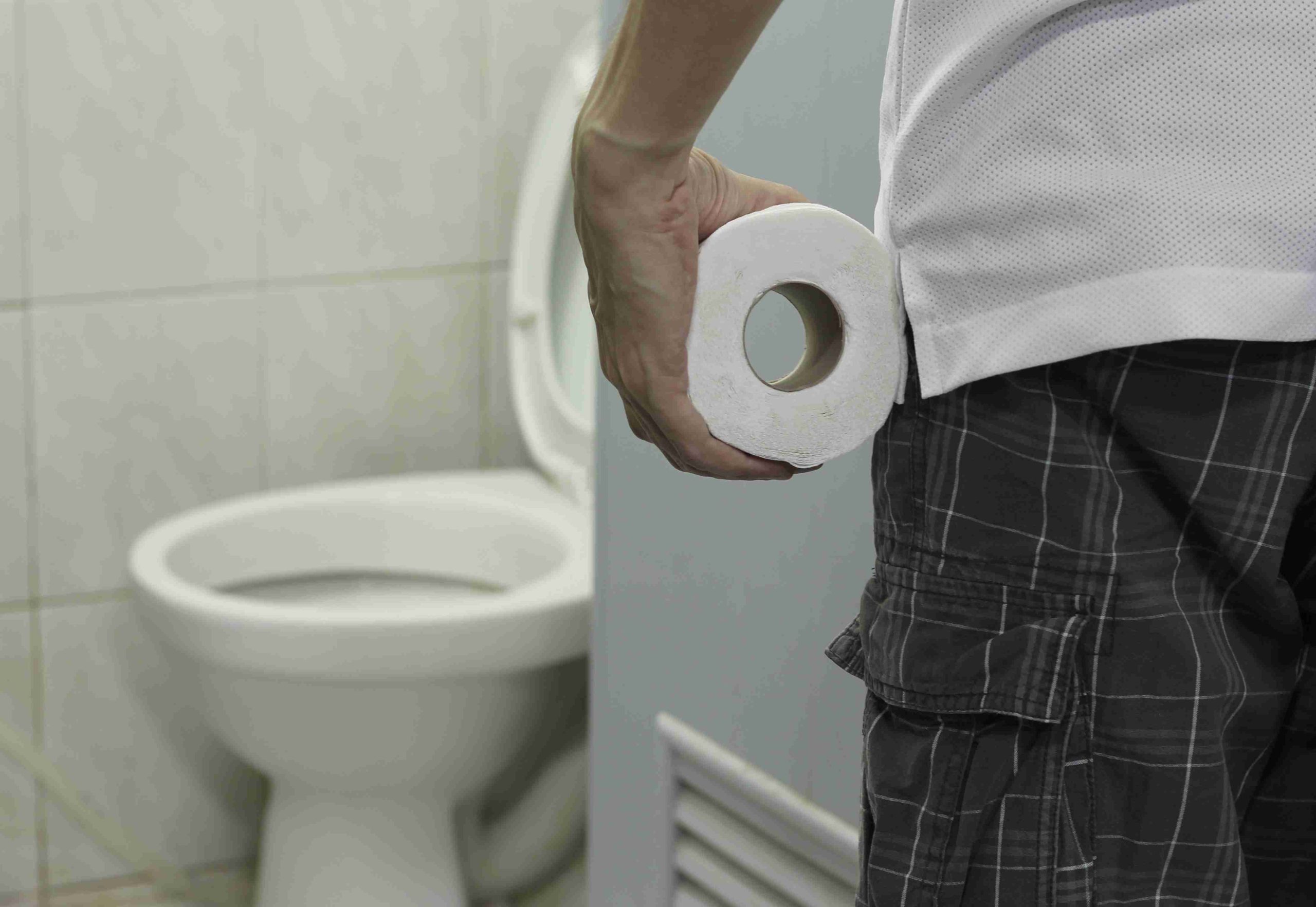 Man holding a tissue facing the toilet bowl.