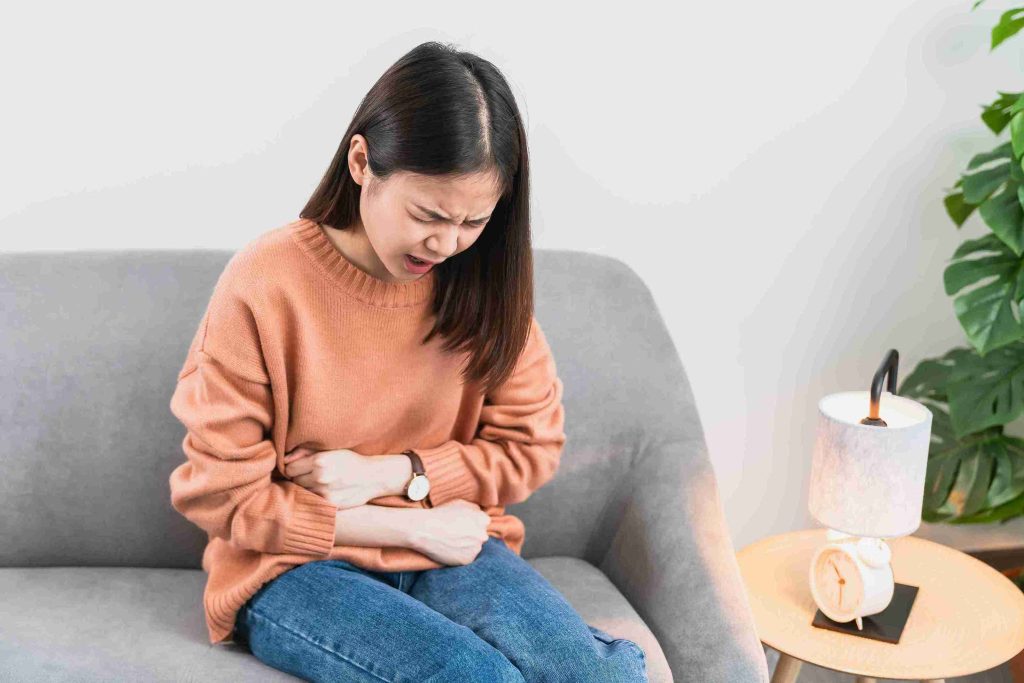 Young woman sitting in the couch with abdominal pain.