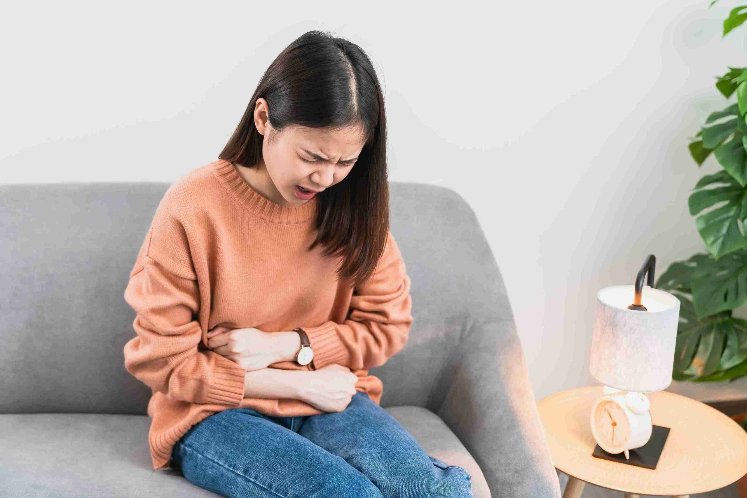 Young woman sitting in the couch with abdominal pain.