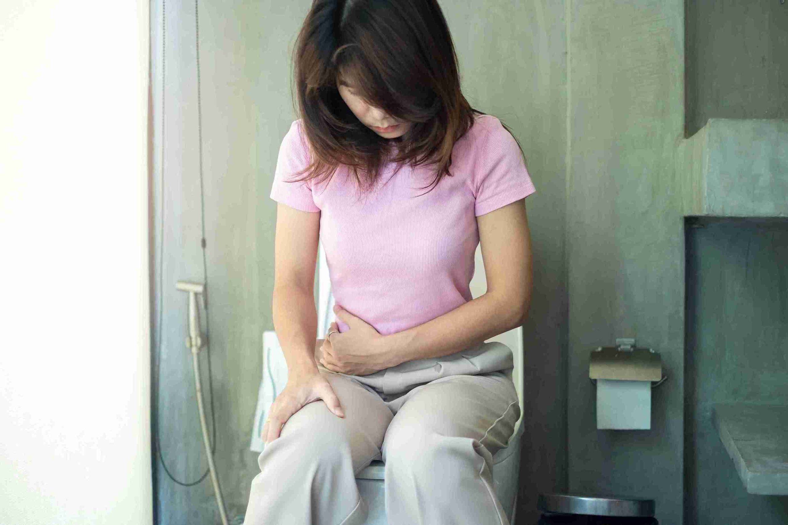 Woman sitting on the toilet bowl with her hand on her stomach.