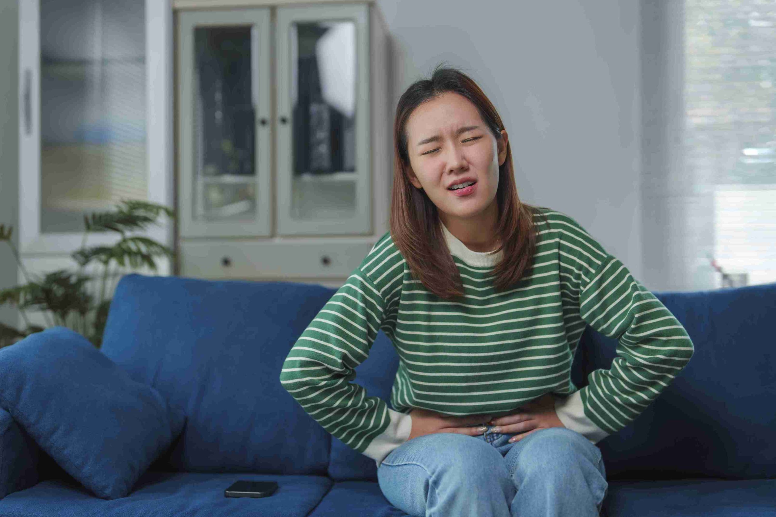 Woman sitting in the couch with her hands on her stomach.
