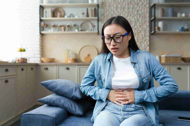 Young woman sitting on the couch with stomach pain.