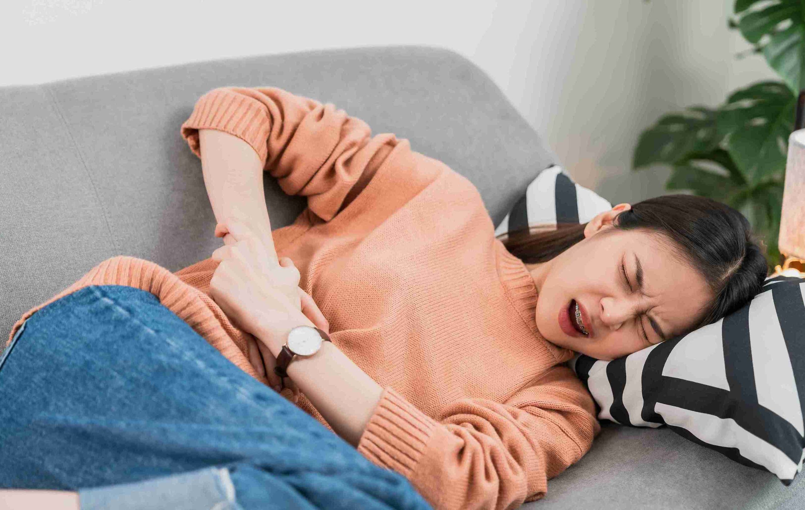 Young woman with stomach pain and her hands on her stomach.