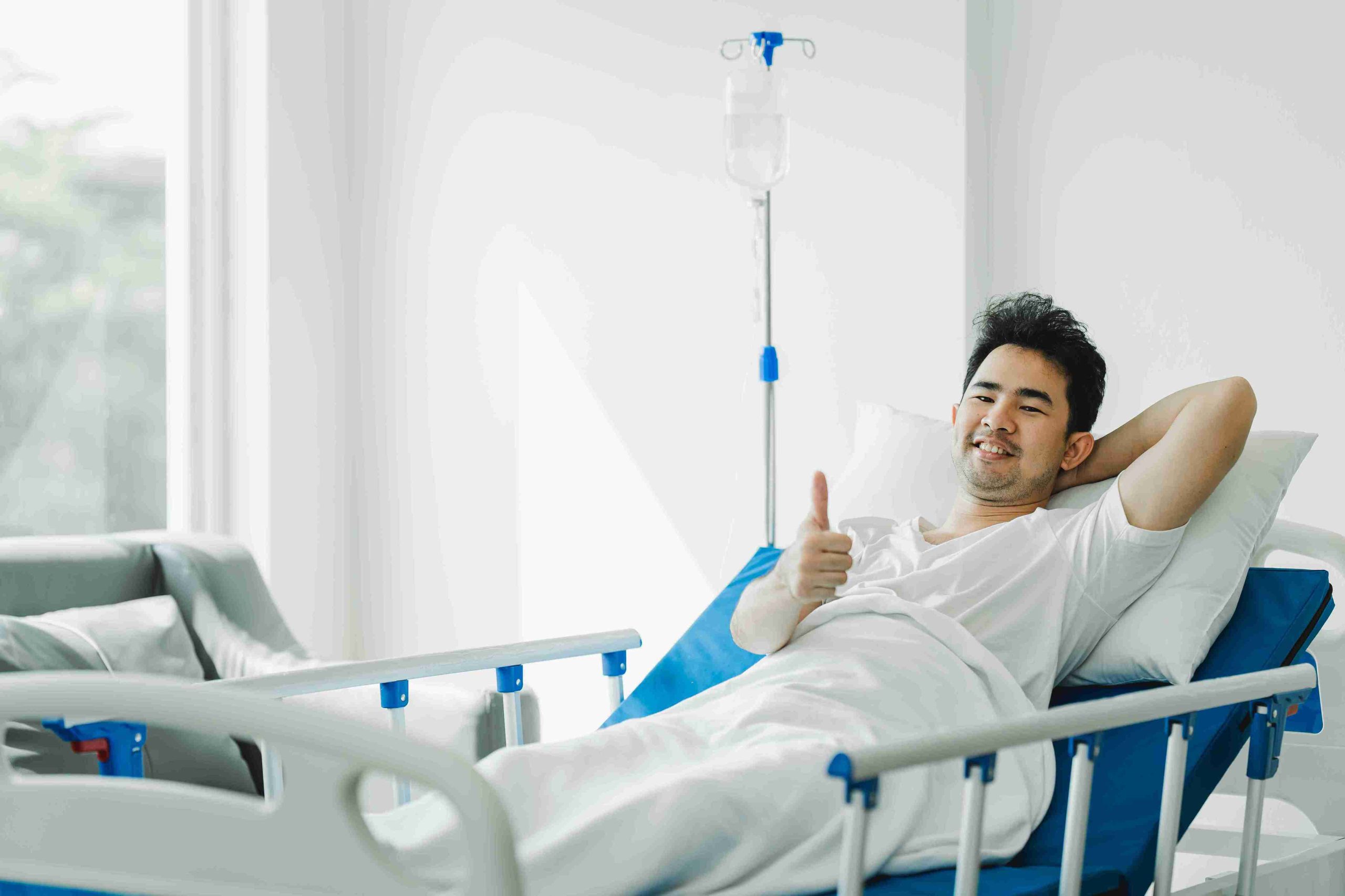 Patient lying in the hospital bed smiling and giving the thumbs up sign.