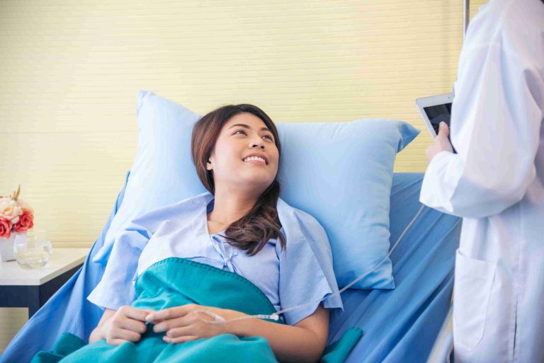 Patient smiling while lying in a hospital bed and talking to her doctor.