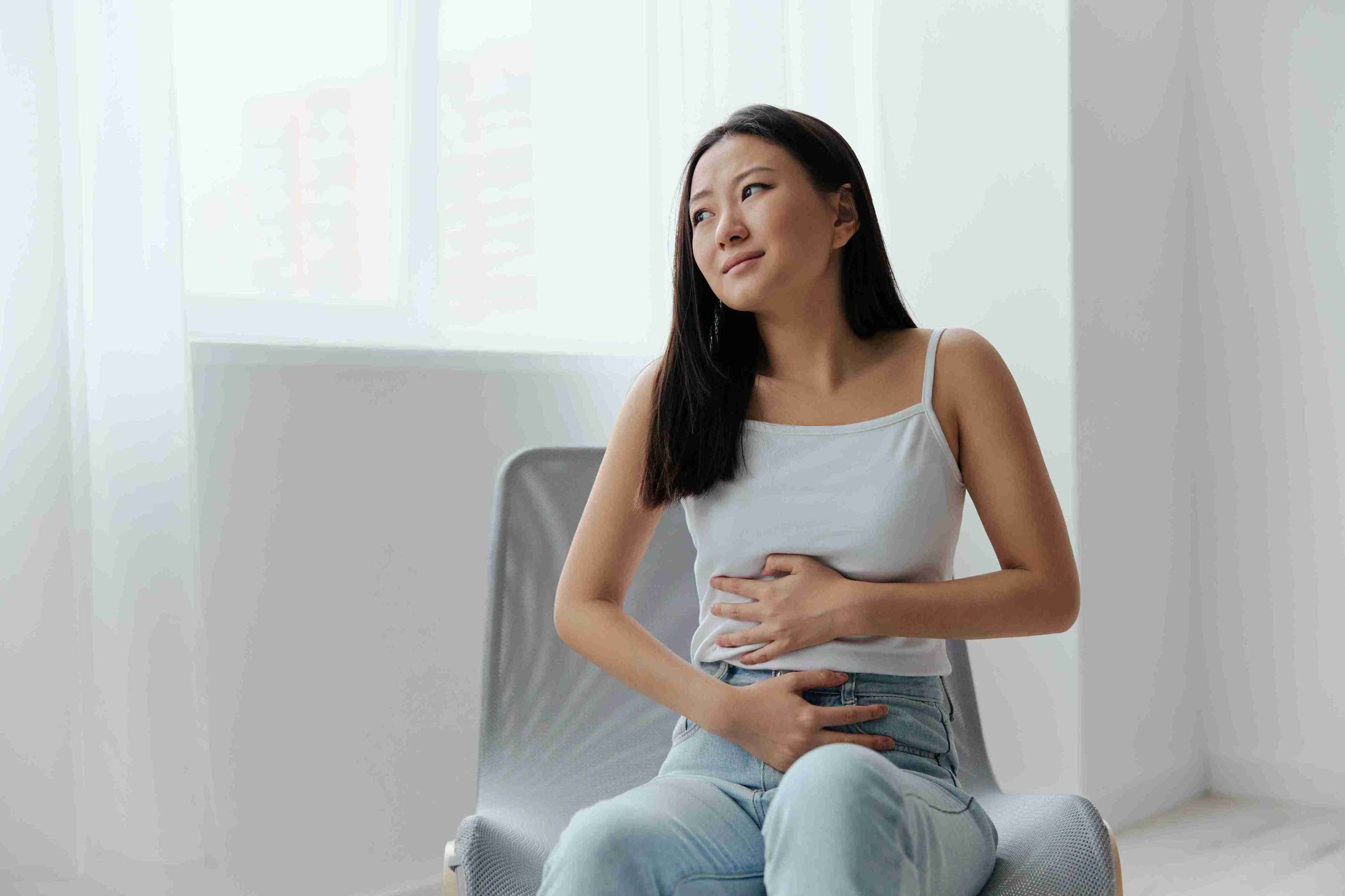 Young woman sitting on a sofa with her hands on her stomach.