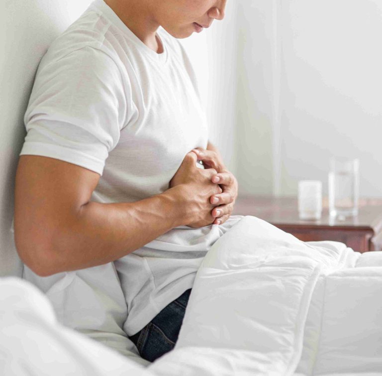 Man sitting on the bed with gastric pain and both hands on his stomach.