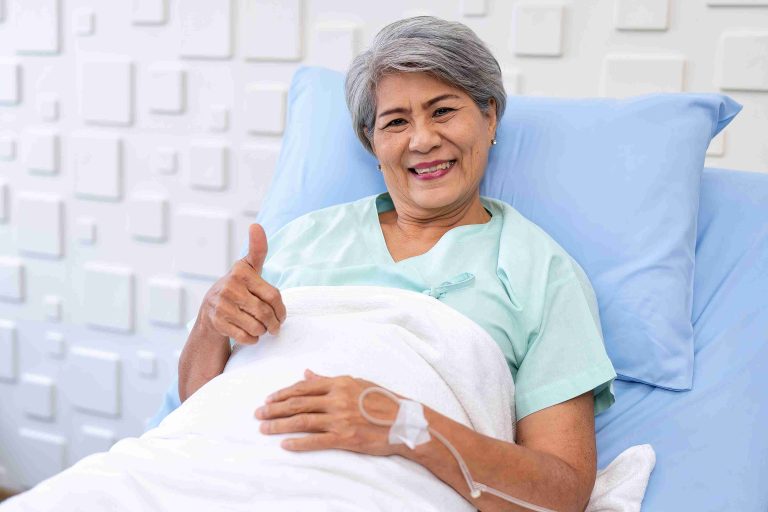 Elderly patient smiling and giving the thumbs up while lying in a hospital bed.