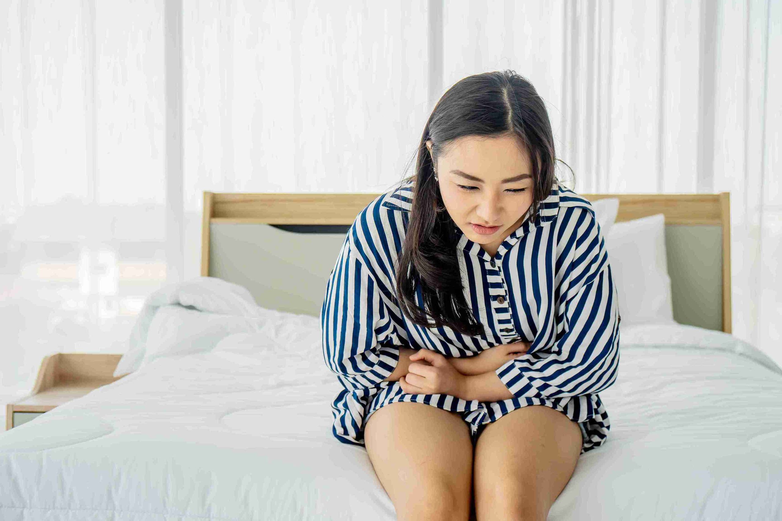 Young woman sitting in her bed with stomach pain.