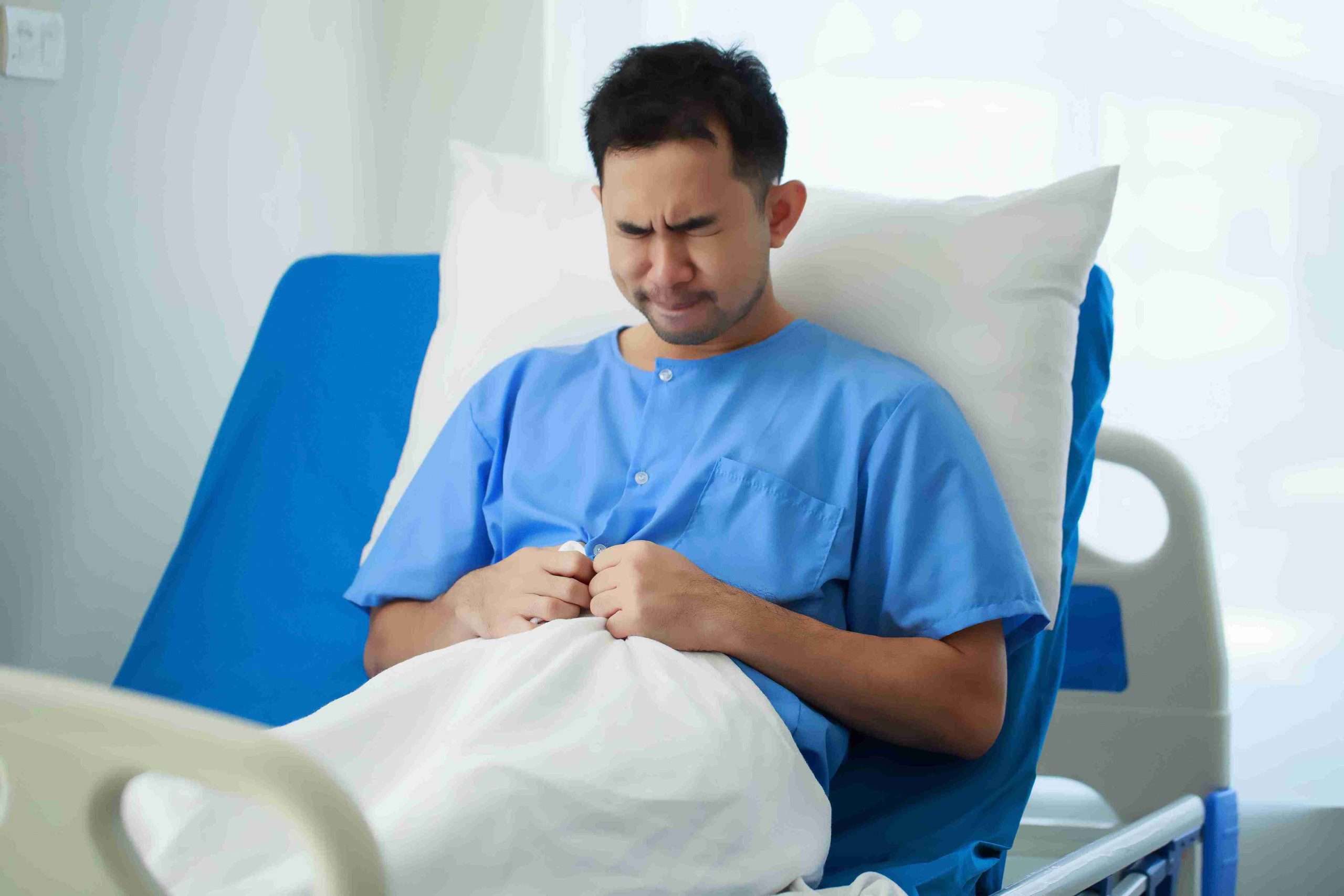 Male patient sitting in the hospital bed with abdominal pain.