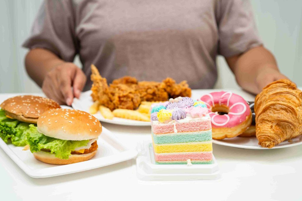 Woman preparing to eat cakes, croissants, chicken, and burgers.