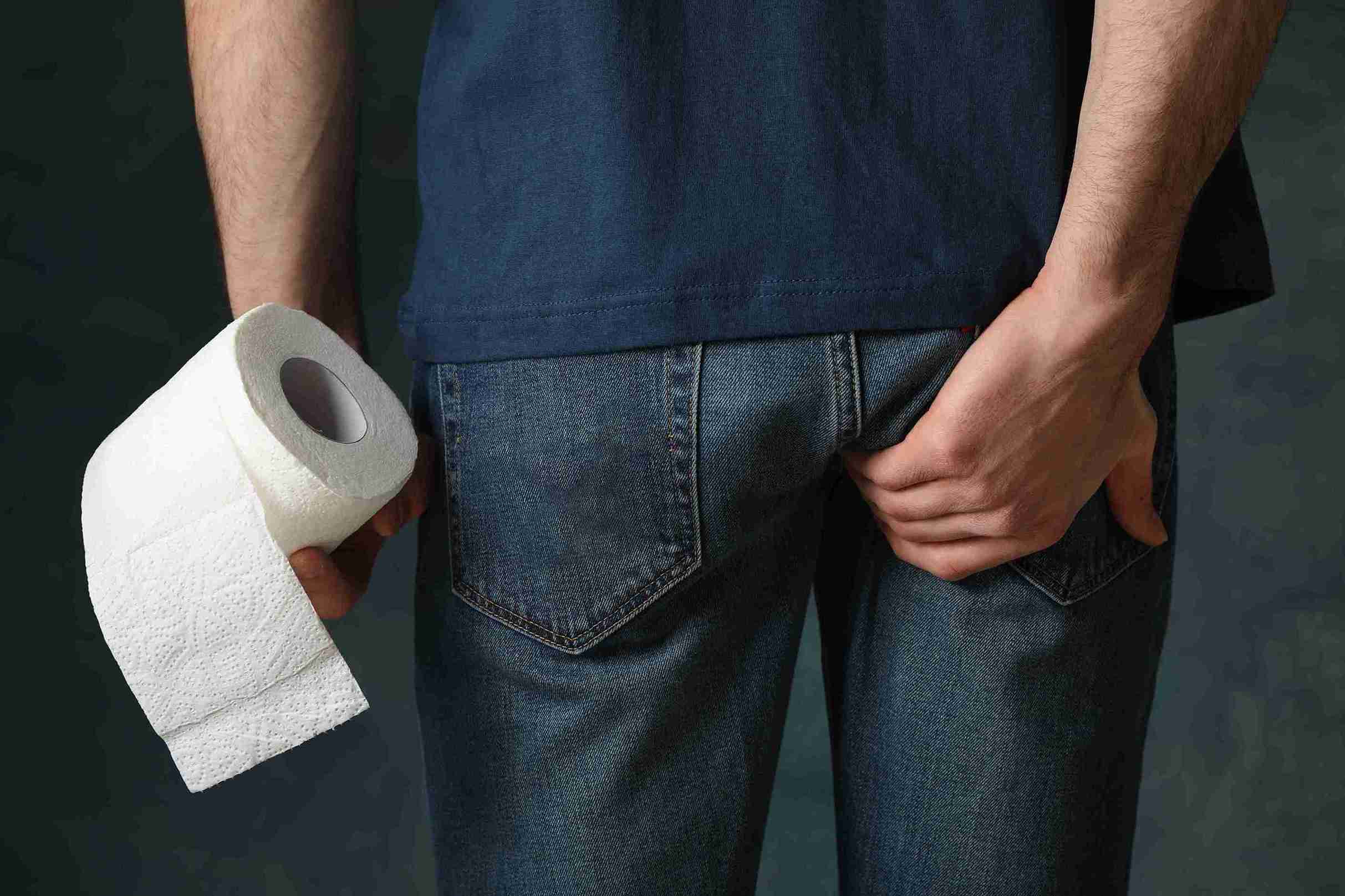 Man holding a roll of toilet tissue on one hand and holding his backside with the other hand.