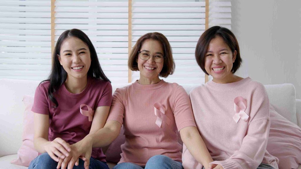 Three smiling women wearing cancer ribbons, smiling at the camera.