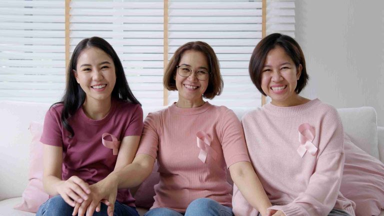 Three smiling women wearing cancer ribbons, smiling at the camera.