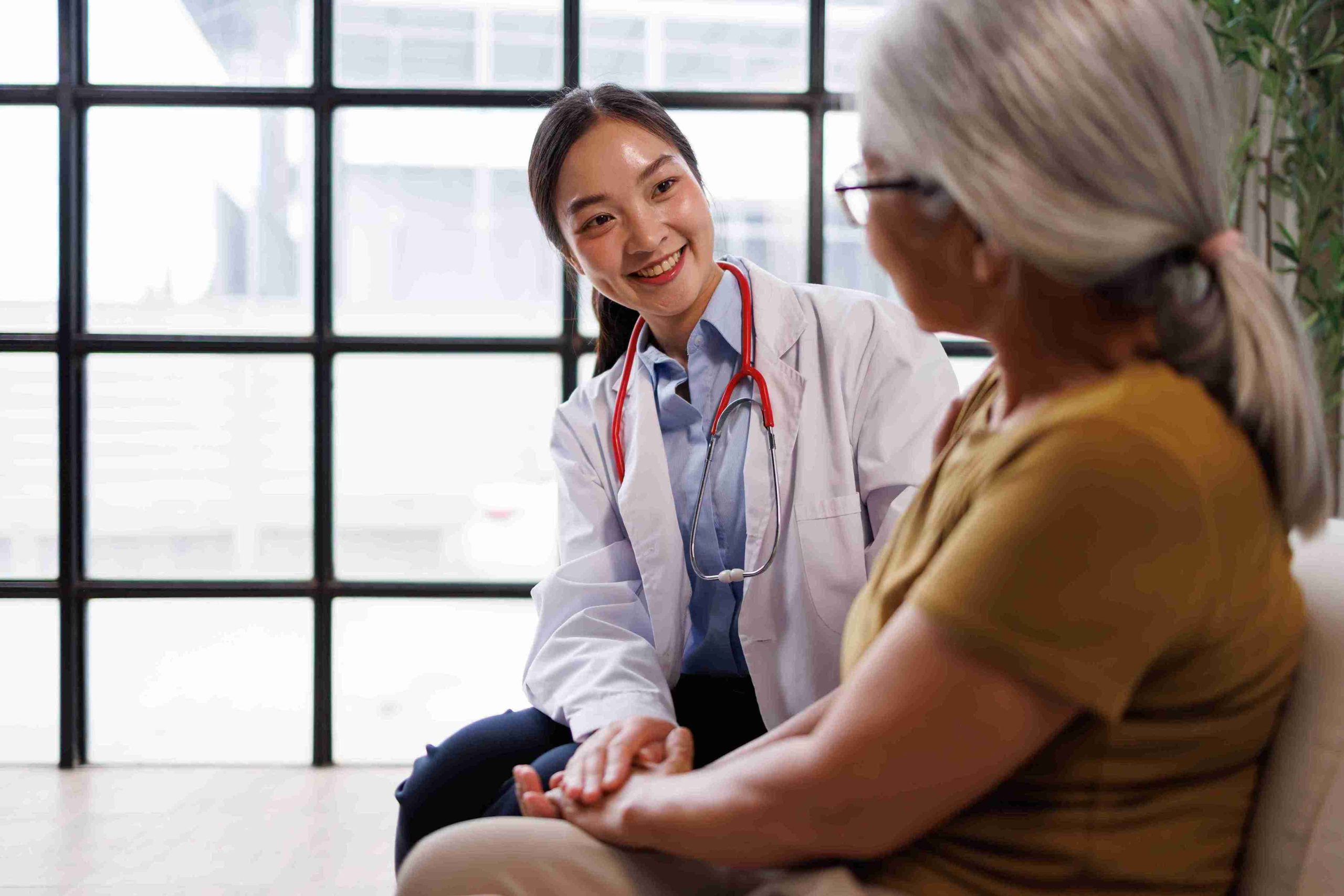 Young doctor smiling and sitting next to an elderly patient.